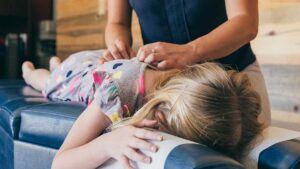 A chiropractor explains a spinal adjustment model to an adult patient in a bright clinic room.