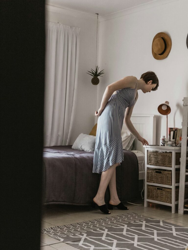 Person performing gentle morning stretches beside a bed in a bright home bedroom.